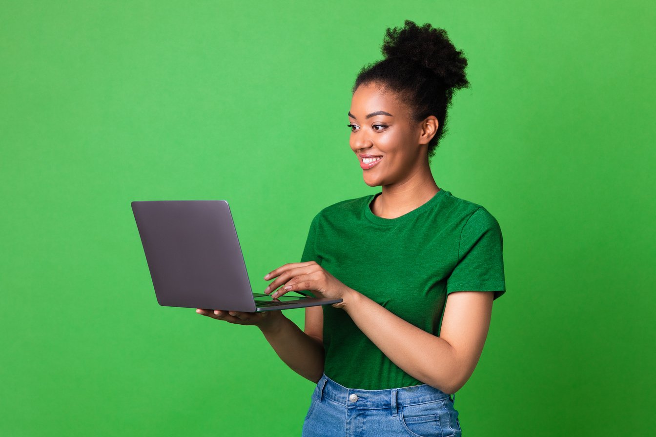 Happy teenager standing with laptop and typing